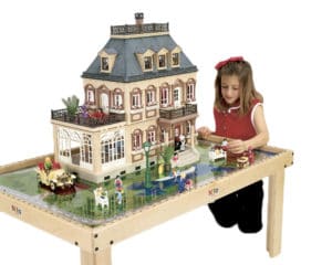 Girl playing with toy figures on Nilo childrens play table while building a barbie play house.